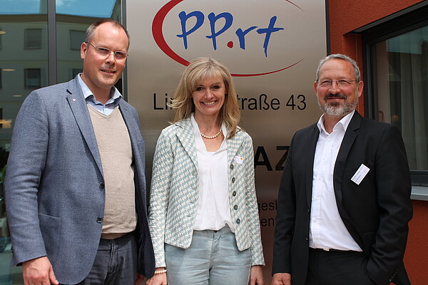 Zwei Herren links und rechts und eine Frau in der Mitte lächeln freundlich in die Kamera. Hinter Ihnen ist ein Aufsteller mit dem Logo PP.rt zu sehen. 