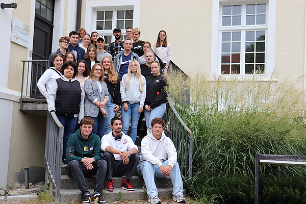 Auf einer Treppe vor einem Gebäude haben sich mehrere junge Menschen für ein Gruppenfoto aufgestellt.