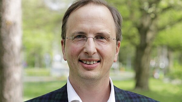 Ein Mann mit Brille, kurzem Haar und einem karierten Jackett. 