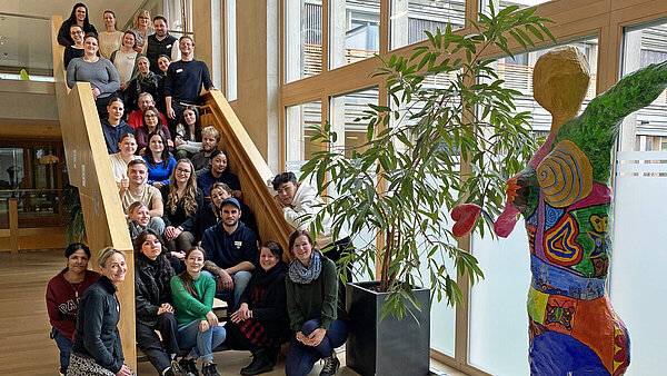 Rund 30 Personen, die alle in Richtung Kamera schauen, stehen und sitzen auf einer Freitreppe im Inneren eines Klinikgebäudes.