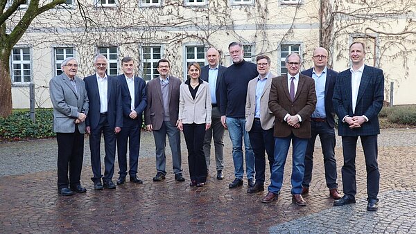 Eine Frau und zehn Männer stehen vor der Fassade eines historischen Gebäudes zum Gruppenbild zusammen und schauen freundlich in Richtung Kamera.