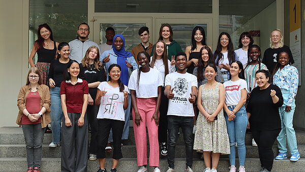 Eine Gruppe junger Menschen steht in mehreren Reihen auf einer Treppe. 