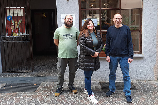 Drei junge Menschen, eine Frau und zwei Männer, stehen vor einer Hausfassade und dem Eingang zum Kontaktladen in Ravensburg.