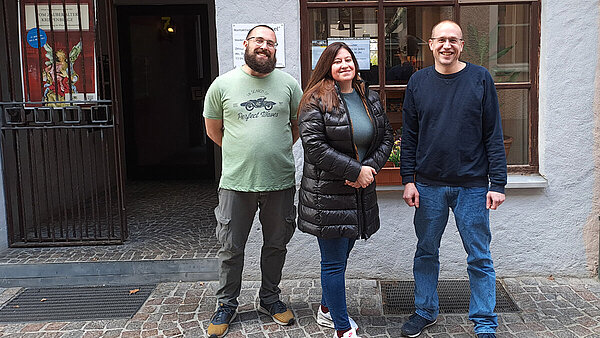 Drei junge Menschen, eine Frau und zwei Männer, stehen vor einer Hausfassade und dem Eingang zum Kontaktladen in Ravensburg.