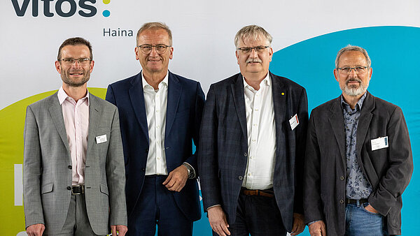 Vier Herren in stehen nebeneinander und schauen freundlich in die Kamera. Im Hintergrund ist das Logo von Vitos zu sehen. 