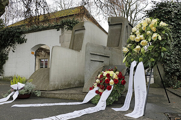 Niedergelegte Blumenkränze umrahmen das Mahnmal der grauen Busse an der alten Pforte des ZfP-Standorts Weissenau.
