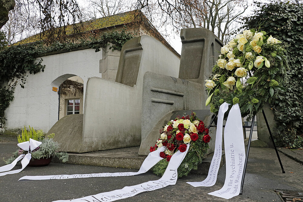 Niedergelegte Blumenkränze umrahmen das Mahnmal der grauen Busse an der alten Pforte des ZfP-Standorts Weissenau.