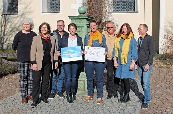 Acht Menschen stehen vor einer Säule, die zwei Damen in der Mitte halten das Zertifikat für rauchfreies Krankenhaus in den Händen