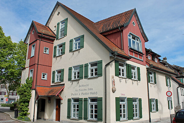 Es ist ein Beiges Gebäude mit grünen Fensterläden und roten Gauben zu sehen.