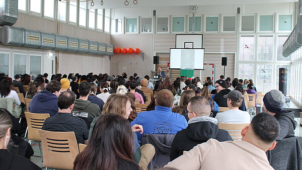 Ein vollbestuhlter Saal, in dem junge Leute sitzen und nach vorne auf die Bühne blicken.