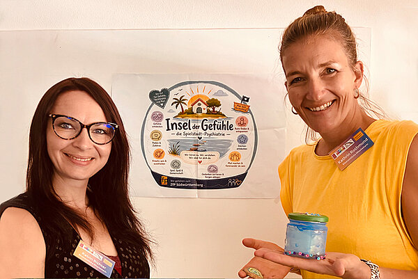 Zwei Frauen stehen vor einem Plakat auf dem "Insel der Gefühle" zu lesen ist.