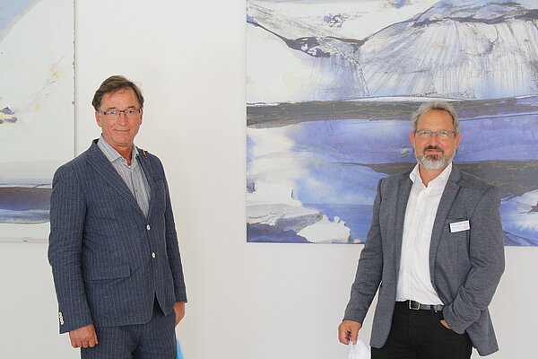 Zwei Herren im Anzug und mit Brille stehen mit Abstand vor einem Gemälde mit den Farbtönen weiß, blau und grau