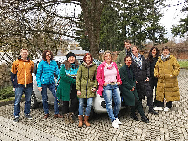 Ein größere Gruppe von Menschen hat sich rund um ein kleines weißes Auto aufgestellt.