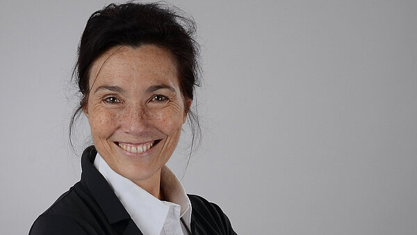 Eine dunkelhaarige Frau mit weißer Bluse, schwarzem Blazer und einer Hochsteckfrisur.