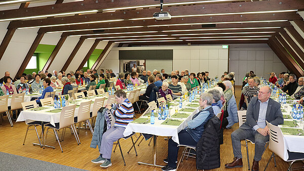 Senioren sitzen an festlich gedeckten Tischen und unterhalten sich. 