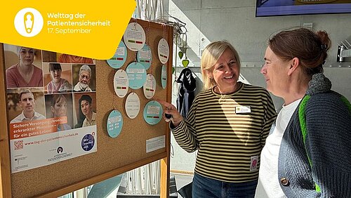 Zwei Frauen stehen, sich unterhaltend, neben einer Stellwand, auf der ein Plakat und ein Quiz zur Patientensicherheit angepinnt sind.