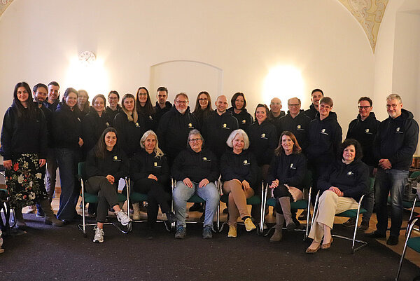 Eine Gruppe von rund 40 Personen sitzt bzw. steht vor einer weißen Wand, alle tragen schwarze Hoodies mit ZfP-Logo.