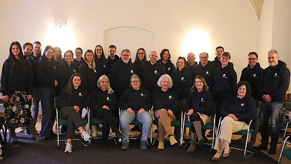 Eine Gruppe von rund 40 Personen sitzt bzw. steht vor einer weißen Wand, alle tragen schwarze Hoodies mit ZfP-Logo.