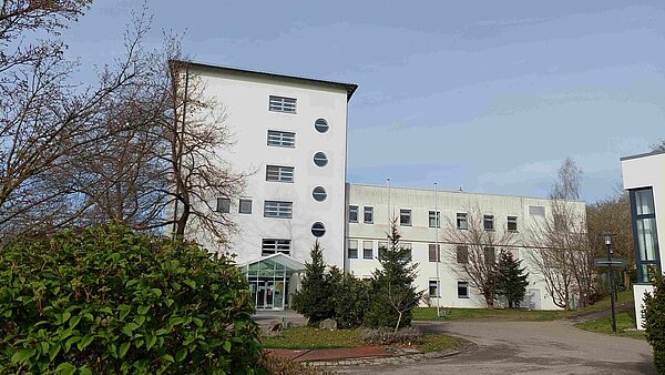 Man sieht ein mehrstöckiges Gebäude mit flachem Dach und weißer Fassade. 