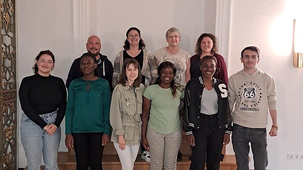 10 junge Männer und Frauen stehen in einer Gruppe zusammen und schauen in Richtung Kamera.