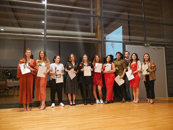 Gruppenaufnahme in einer Turnhalle. Elf junge Personen lächeln freundlich in die Kamera und halten eine Rose und eine Urkunde in der Hand