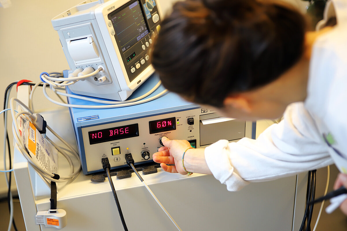 Eine Frau in weißem Kittel beugt sich über ein EEG-Gerät und dreht an einem Knopf.