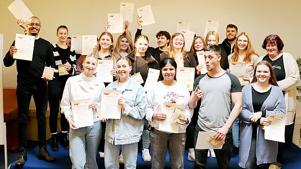Circa 20 junge Menschen halten lächelnd ihre Zertifikate in die Kamera.