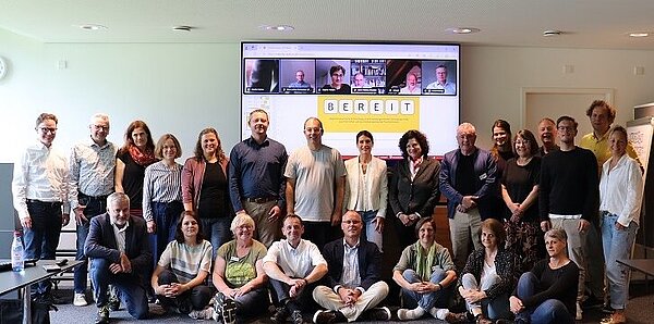 Mehrere Frauen und Männer in Alltagskleidung stehen hinter und vor einer roten Empfangstheke. 