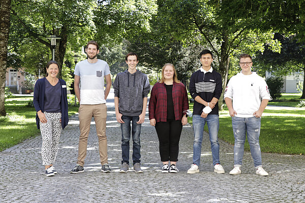 Sechs freundliche junge Menschen stehen nebeneinander im Park.