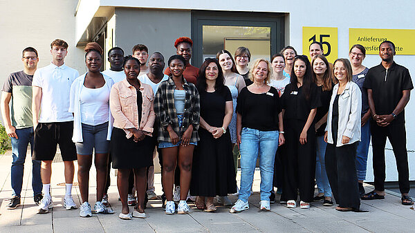 Rund zwanzig Personen haben sich zum Gruppenbild vor einem weißen Gebäude aufgestellt. 