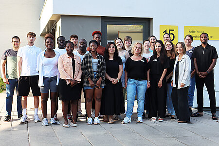 Rund zwanzig Personen haben sich zum Gruppenbild vor einem weißen Gebäude aufgestellt. 