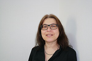 Portraitbild von Frau Sabine Genannt-Kroner, einer Frau mittleren Alters mit langen braunen Haare und Brille.