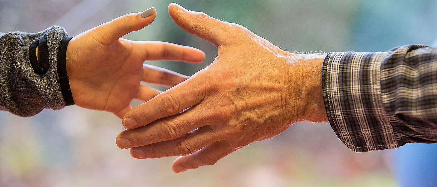 Zwei Hände, die sich einander entgegenstrecken und eine Geste der Hilfsbereitschaft symbolisieren.
