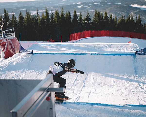 Junger Snowboarder fahrt bei strahlendem Sonnenschein die Piste hinunter