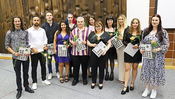 12 junge Männer und Frauen, allesamt frisch examinierte Pflegefachpersonen, stehen in festlicher Kleidung in einer Gruppe zusammen und schauen in Richtung Kamera.