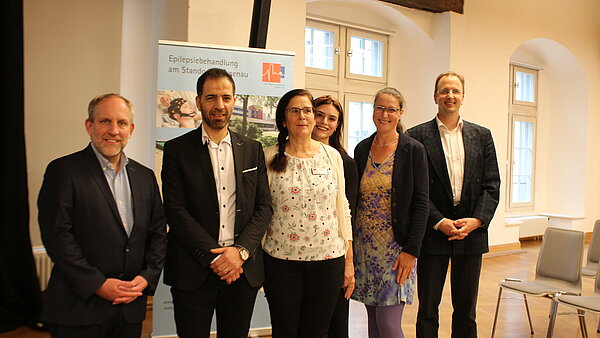 Drei Männer und drei Frauen stehen nebeneinander, im Hintergrund ist ein Banner mit dem Logo der Epilepsie-Akademie erkennbar. 