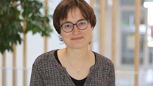 Portrait einer Frau lächelnden Frau mit kurzen braunen Haaren und Brille.