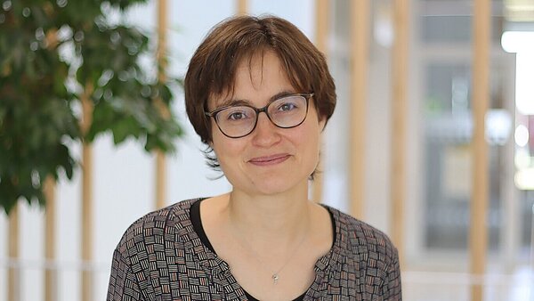 Portrait einer Frau lächelnden Frau mit kurzen braunen Haaren und Brille.