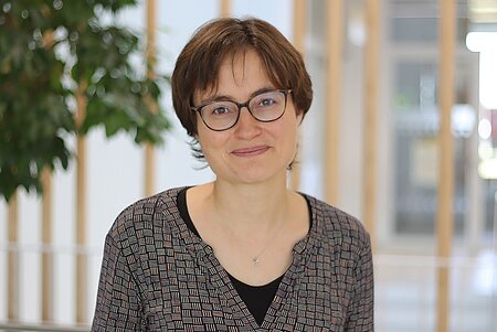 Portrait einer Frau lächelnden Frau mit kurzen braunen Haaren und Brille.