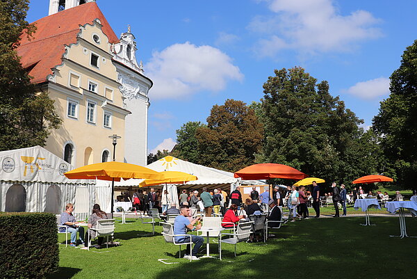 Gartenfest bei gutem Wetter mit vielen Besuchern. Mit Festzelt, Stehtische und schönen Sitzgelegenheiten unterm Sonnenschirm.