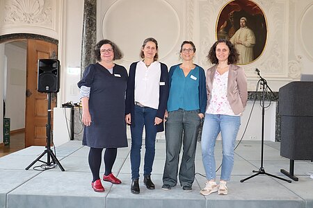 Vier Frauen stehen nebeneinander auf der Bühne des Klosterfestsaals im ZfP Südwürttemberg in Weissenau.