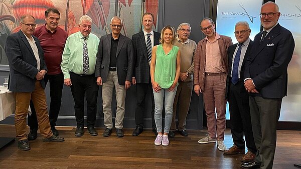 Zehn Männer und Frauen stehen in einem Halbkreis nebeneinander.