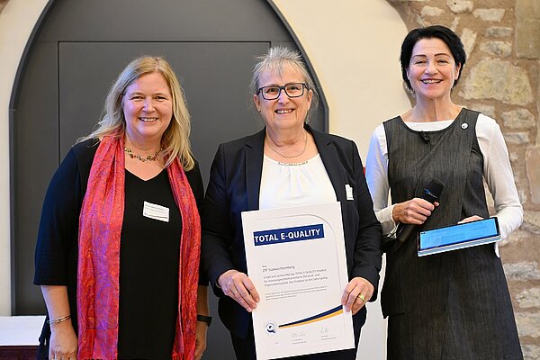 Drei Frauen stehen nebeneinander, die Dame in der Mitte hält eine Urkunde in den Händen. 