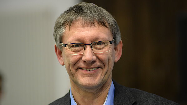 Portraitfoto Dr. Jochen Tenter, ein Mann Mitte 60 im Anzug mit graubraunen Haaren und Brille lächelt in die Kamera.