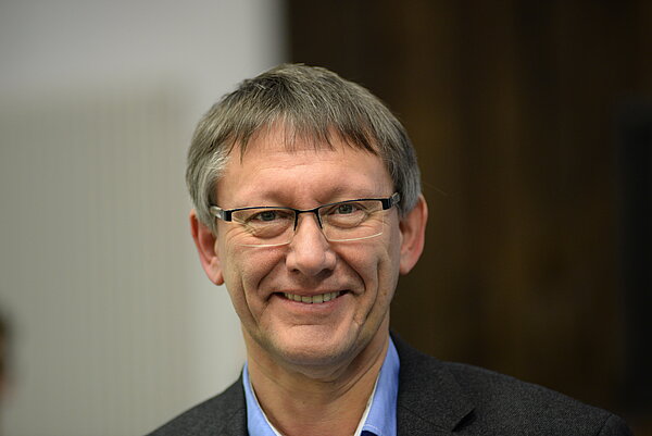Portraitfoto Dr. Jochen Tenter, ein Mann Mitte 60 im Anzug mit graubraunen Haaren und Brille lächelt in die Kamera.