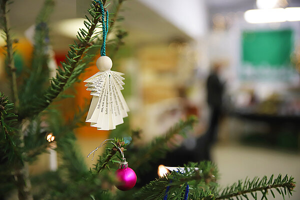 Nahaufnahme eines Papierengels, der am Zweig eines Weihnachtsbaums hängt; der Hintergrund ist unscharf.