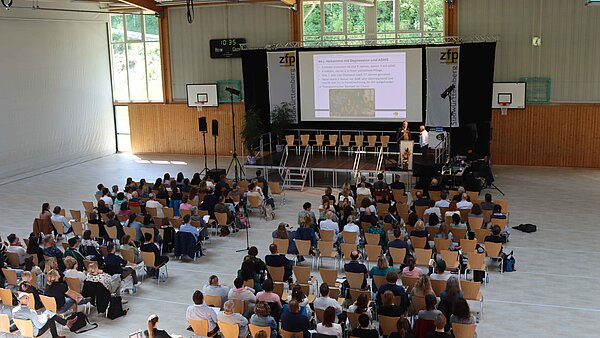 Eine Halle aus der Vogelperspektive, es sitzen Menschen auf Stuhlreihen vor einer Bühne. 