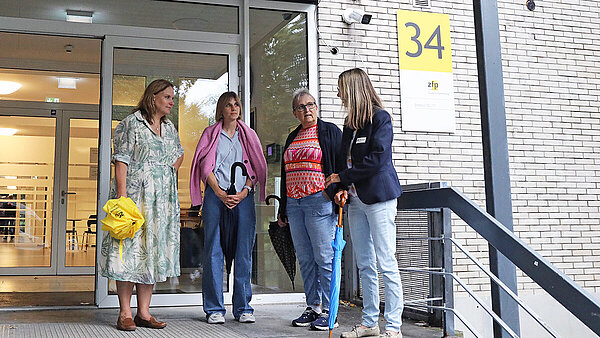 Vier Frauen stehen beisammen und unterhalten sich vor dem überdachten Eingang eines Klinikgebäudes.