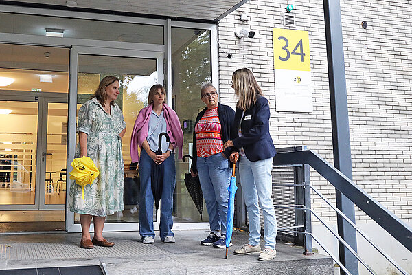 Vier Frauen stehen beisammen und unterhalten sich vor dem überdachten Eingang eines Klinikgebäudes.