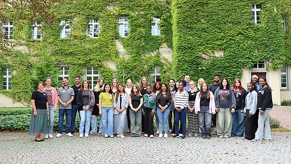 Eine große Gruppe jüngerer Menschen steht vor einer mit Efeu bewachsenen Hauswand.